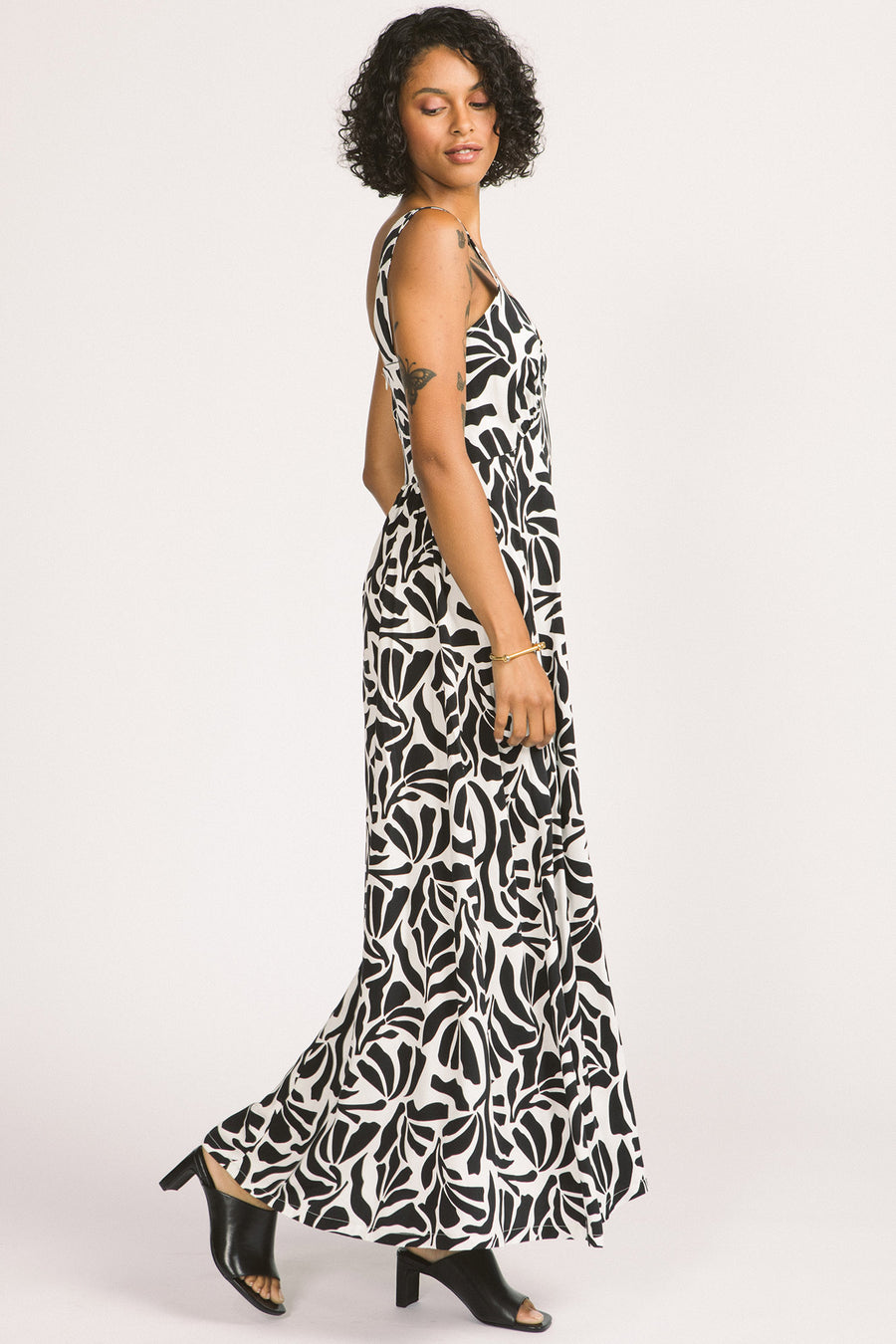Side view of woman wearing black and white leaf print Alora maxi dress by Allison Wonderland. 