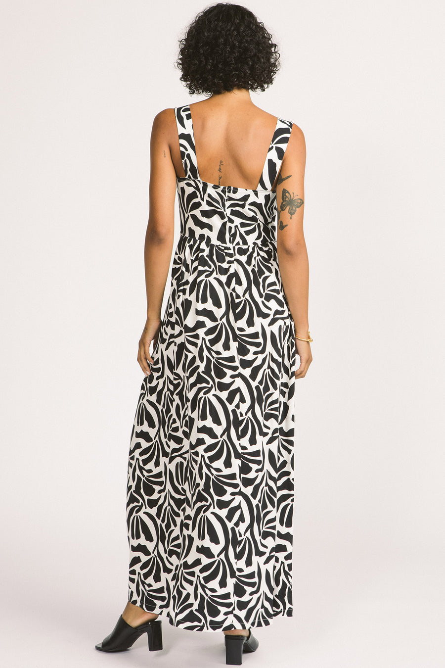 Back view of woman wearing black and white leaf print Alora maxi dress by Allison Wonderland. 