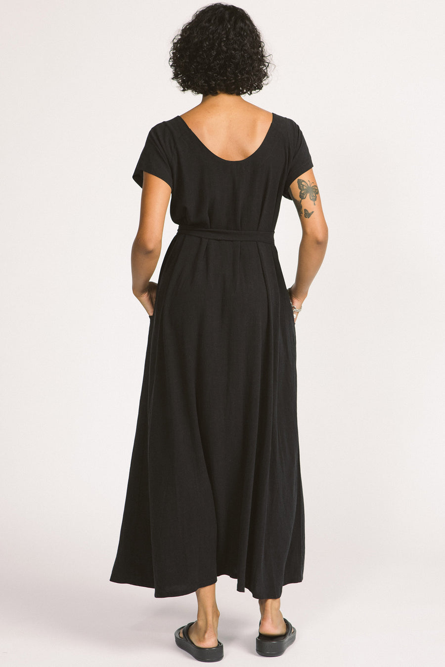 Back view of woman wearing black maxi Allison Wonderland Enola Dress tied at waist. 