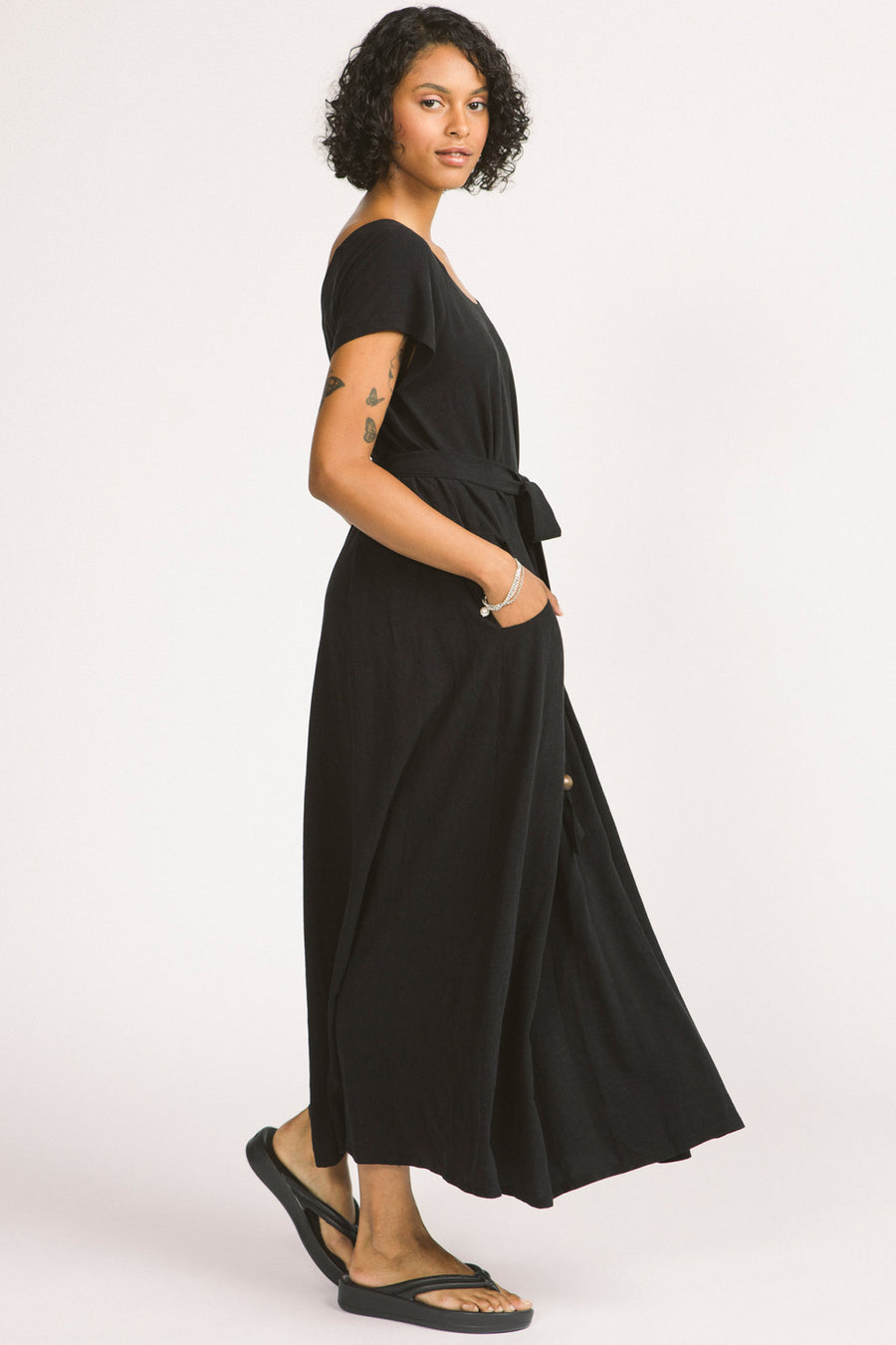 Side view of woman wearing black maxi Allison Wonderland Enola Dress tied at waist. 