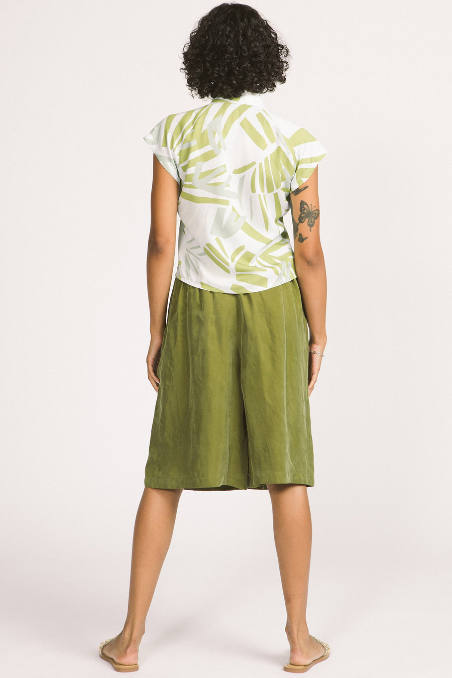 Back view of woman wearing a green and white leaf print Isabeau blouse by Allison Wonderland. 