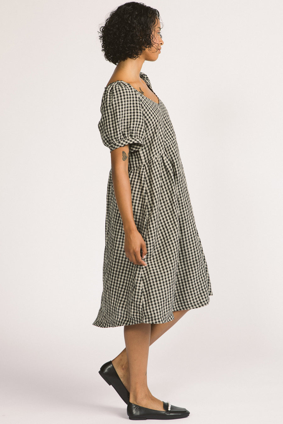 Side view of woman wearing black and white linen gingham oversized babydoll Verity dress. 
