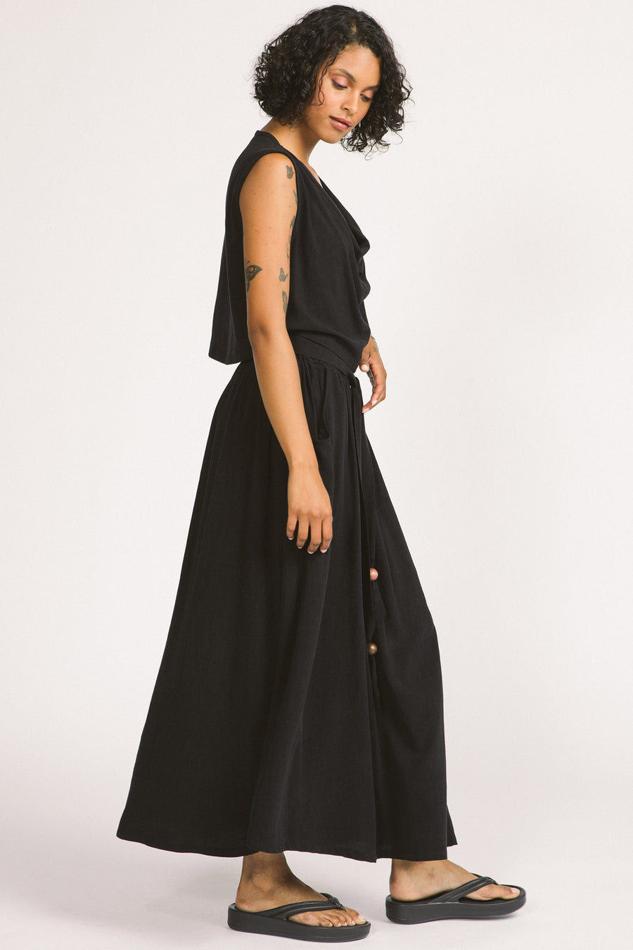 Side view of woman wearing black cowl neck sleeveless Kiko blouse by Allison Wonderland. 