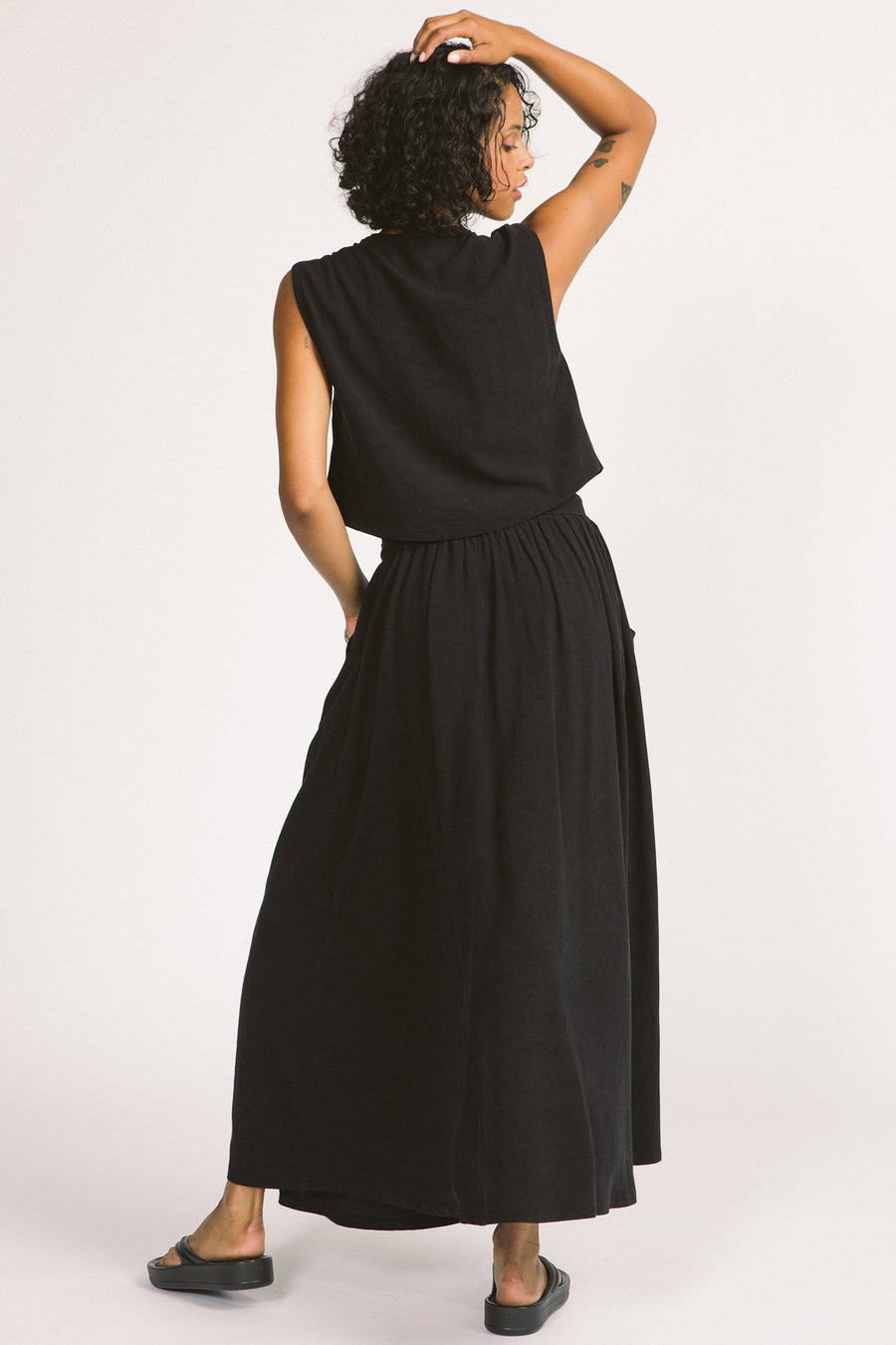 Back view of woman wearing black cowl neck sleeveless Kiko blouse by Allison Wonderland. 